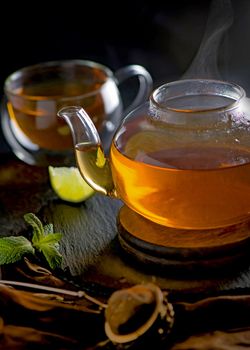 Teapot with tea surrounded with green leaves, tea ceremony, green tea in a transparent cup