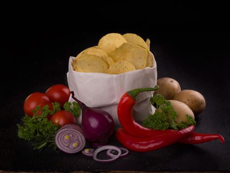 Crispy potato chips in a bag on dark table.