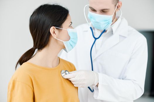 doctor with stethoscope listens to heartbeat of patient wearing medical mask in hospital. High quality photo