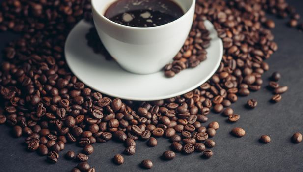 coffee beans and a cup on a white saucer dark background drink. High quality photo