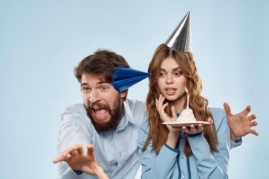 Cheerful man and woman blowing out cake candles holiday decoration blue background. High quality photo