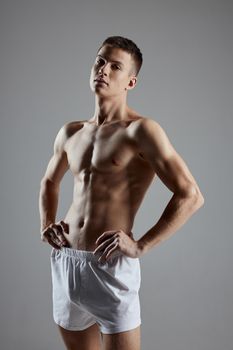 a guy with an athletic physique in shorts holds his hands on the belt on a gray background. High quality photo