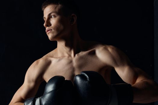 muscular boxer in black gloves on a dark background looking to the side . High quality photo