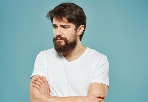 a man in a white t-shirt on a blue background gestures with his hands sad look. High quality photo