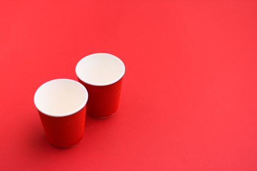 Two empty red paper cups. On a red background. Disposable eco-friendly glasses. copy space