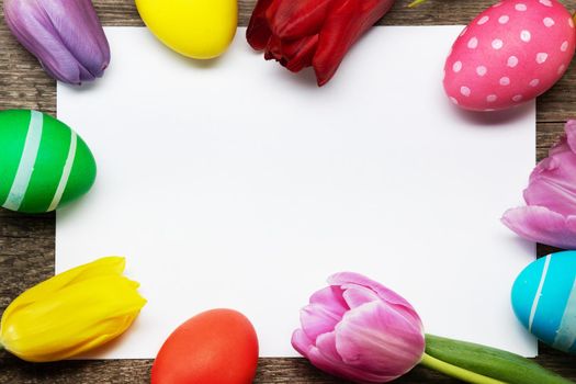 Hand-painted easter eggs with tulips on blank greeting card over wooden background copy space for text