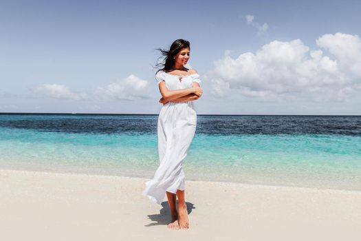 Woman in white dress walking on tropical beach, tropical sea on background