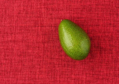 Avocado. The ripe fruit is green, on a red background, isolated, close-up. High quality photo