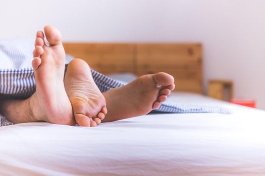 Close up a couples uncovered feet sleeping in bed, morning