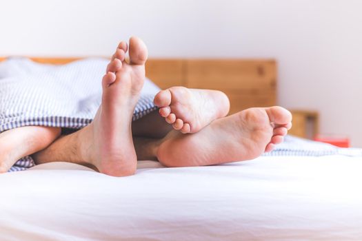 Close up a couples uncovered feet sleeping in bed, morning