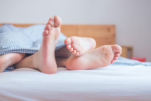 Close up a couples uncovered feet sleeping in bed, morning