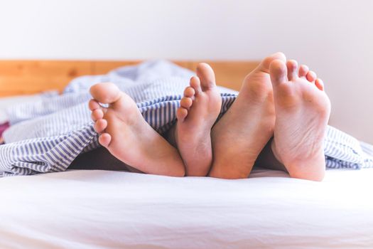Close up a couples uncovered feet sleeping in bed, morning