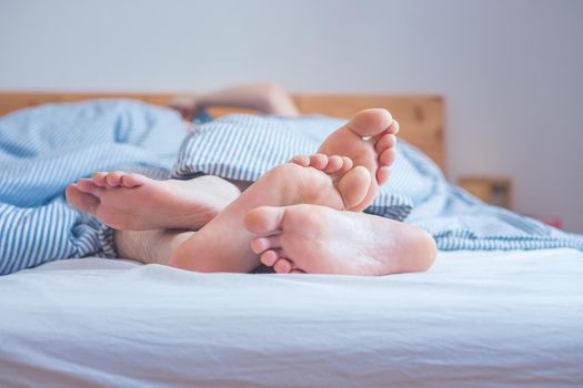 Close up a couples uncovered feet sleeping in bed, morning