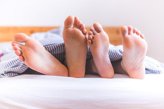 Close up a couples uncovered feet sleeping in bed, morning