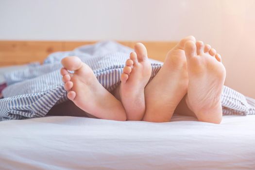 Close up a couples uncovered feet sleeping in bed, morning