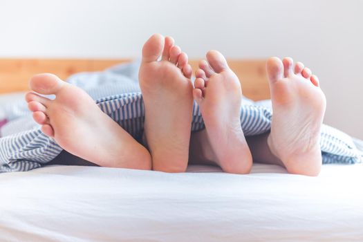 Close up a couples uncovered feet sleeping in bed, morning