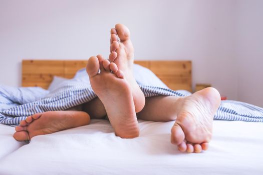 Close up a couples uncovered feet sleeping in bed, morning