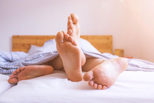 Close up a couples uncovered feet sleeping in bed, morning