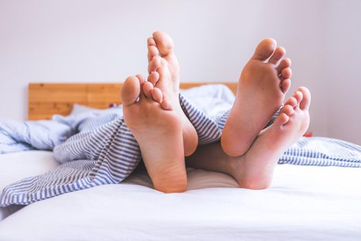 Close up a couples uncovered feet sleeping in bed, morning