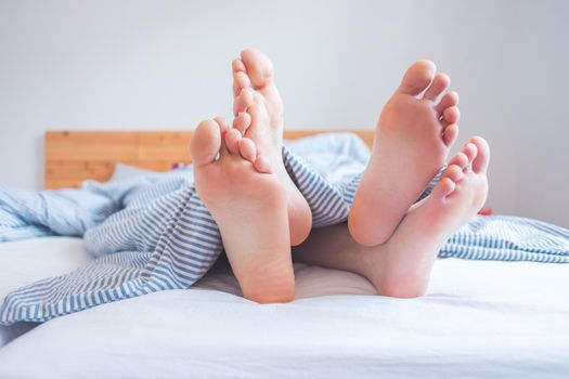 Close up a couples uncovered feet sleeping in bed, morning
