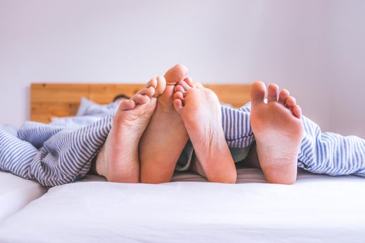 Close up a couples uncovered feet sleeping in bed, morning