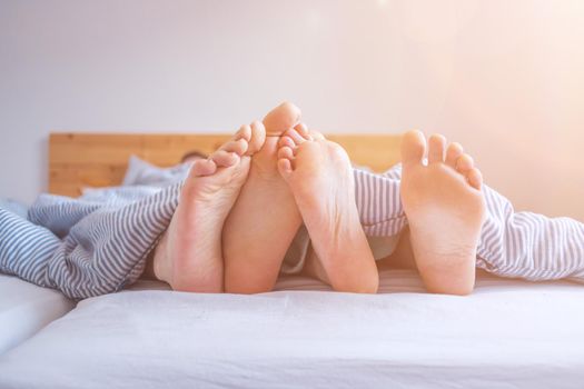 Close up a couples uncovered feet sleeping in bed, morning