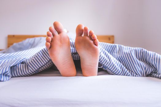 Close up uncovered female adult feet sleeping in bed, morning