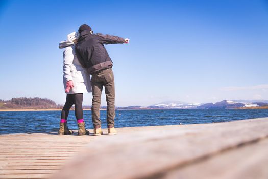 Young couple is standing on a footbridge and enjoys the view over the lake, winter time