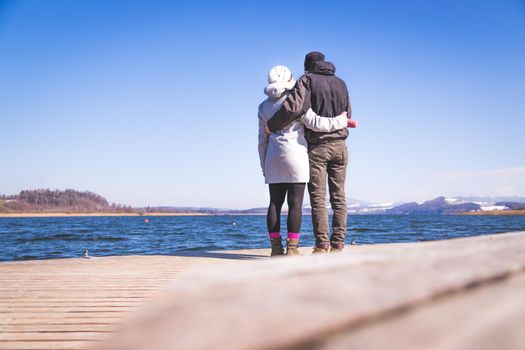 Young couple is standing on a footbridge and enjoys the view over the lake, winter time