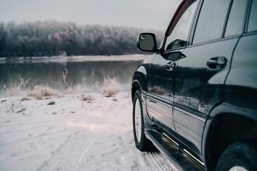 black car near the river on a snowy road and forest in the background. High quality photo