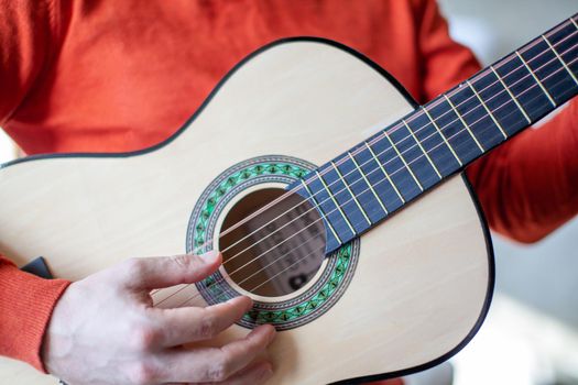 Close-up of a guitar player or a person learning to play an acoustic guitar. Home learning to play a musical instrument