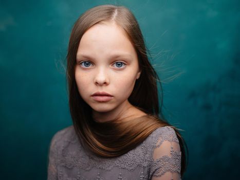 Beautiful little girl in a gray dress close-up cropped view blond hair turquoise background. High quality photo