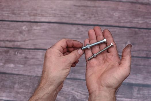 Bolts with nuts in their hands. Working men's hands are dirty from work. Close-up. On a wooden background.