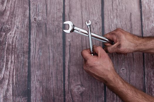 Chrome-plated wrenches in a man's work-smeared hands. On a wooden background. Close-up. copy space