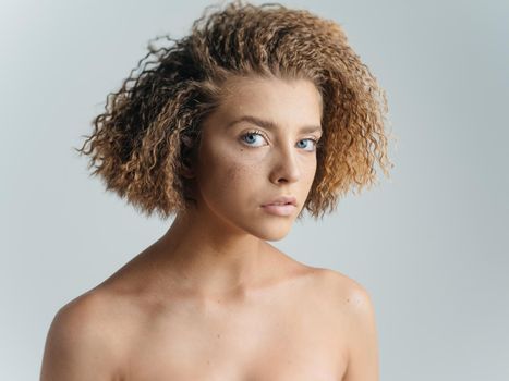 Beautiful woman portrait light background bared shoulders curly hair. High quality photo