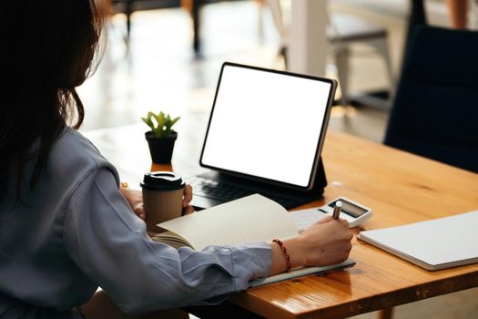 Business woman hand writing on notebook, work on laptop computer with calculator on the desk at modern home office. Online working, work at home concept.