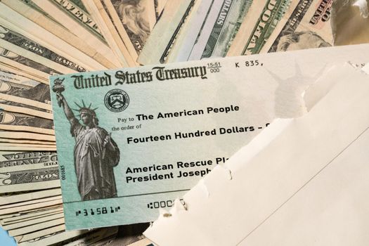 Stack of 20 dollar bills with US Treasury illustrative check to illustrate American Rescue Plan Act of 2021 payment on cash background