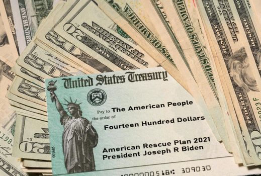 Stack of 20 dollar bills with US Treasury illustrative check to illustrate American Rescue Plan Act of 2021 payment on cash background