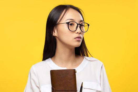 woman of asian appearance with notepad in hand glasses elegant style manager yellow background. High quality photo