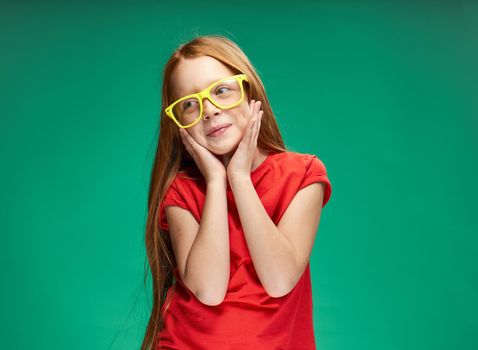 cute red-haired girl gesturing with her hands childhood green background school. High quality photo