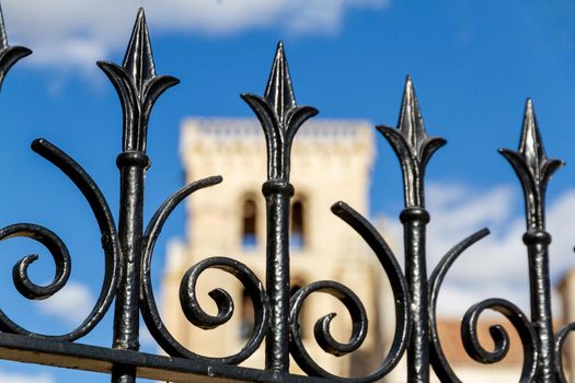 Detail of a black iron fence against a blue sky with an old church tower in the background