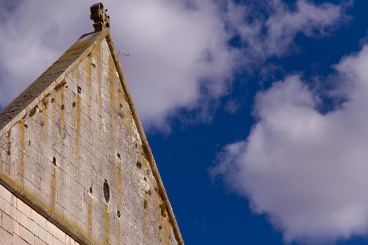 Close-up of a triangular stone wall with a cross on the top against a blue sky