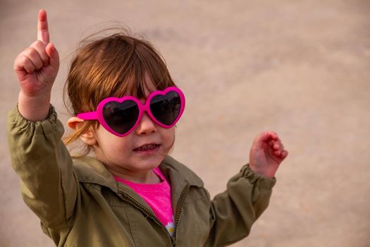 A cute, brown-haired baby girl wearing pink sunglasses and a green jacket