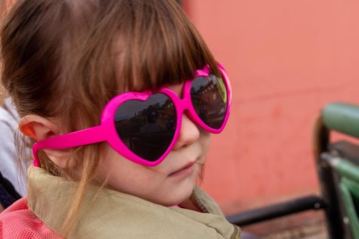 A cute, brown-haired baby girl wearing pink sunglasses and a green jacket