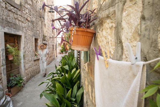 Beautiful blonde young female traveler wearing straw sun hat sightseeing and enjoying summer vacation in an old traditional costal town at Adriatic cost, Croatia.