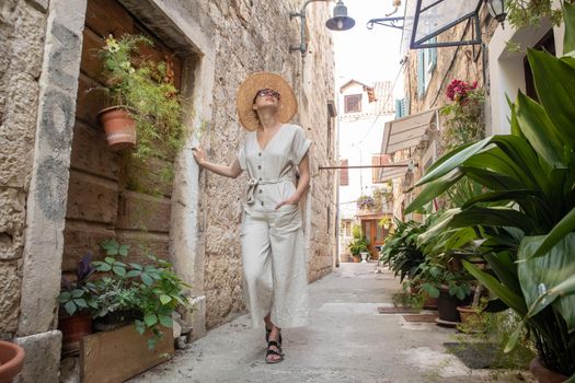 Beautiful blonde young female traveler wearing straw sun hat sightseeing and enjoying summer vacation in an old traditional costal town at Adriatic cost, Croatia