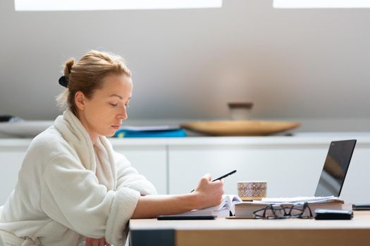 Young businesswoman wearing cosy warm bathrobe working remotly from home in winter Christmas time during 2020 corona virus pandemic. Work from home, selter in place, concept.