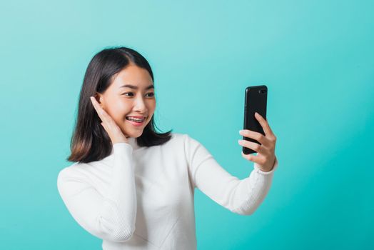 Beautiful Asian woman smile she using a smartphone to selfie photo, happy female photography by mobile phone on mobile phone isolated on a blue background, Technology concept