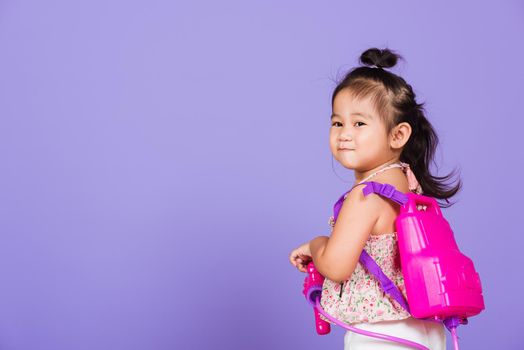 Thai child funny hold toy water pistol and smile, Happy Asian little girl holding plastic water gun, studio shot isolated on purple background, Thailand Songkran festival day national culture concept