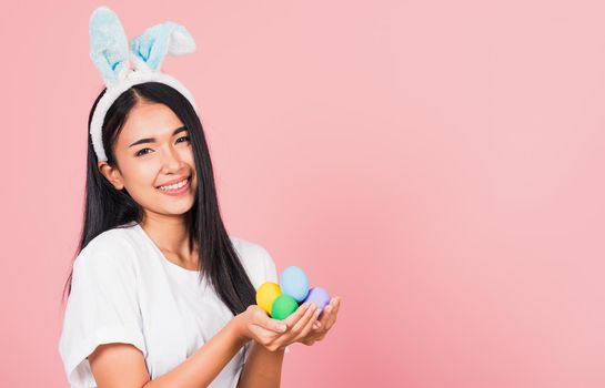 Happy Easter concept. Beautiful young woman smiling wearing rabbit ears holding colorful Easter eggs gift on hands, Portrait female looking at camera, studio shot isolated on pink background
